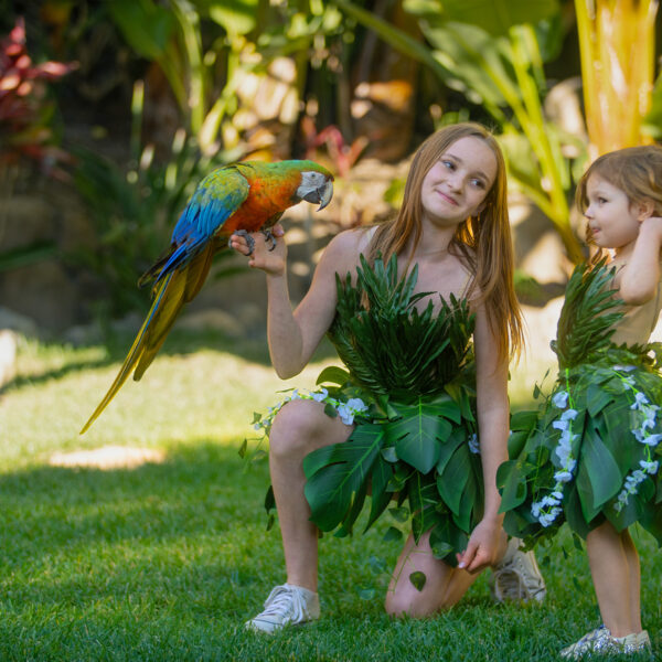 Two girls holding a parrot in a lush Palm Grove at Tropic Shots production set