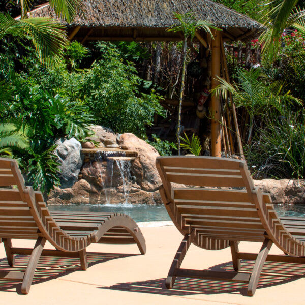 Empty recliner chairs, sitting in front of pool with waterfall and dense jungle foliage in background at Tropic Shots production set
