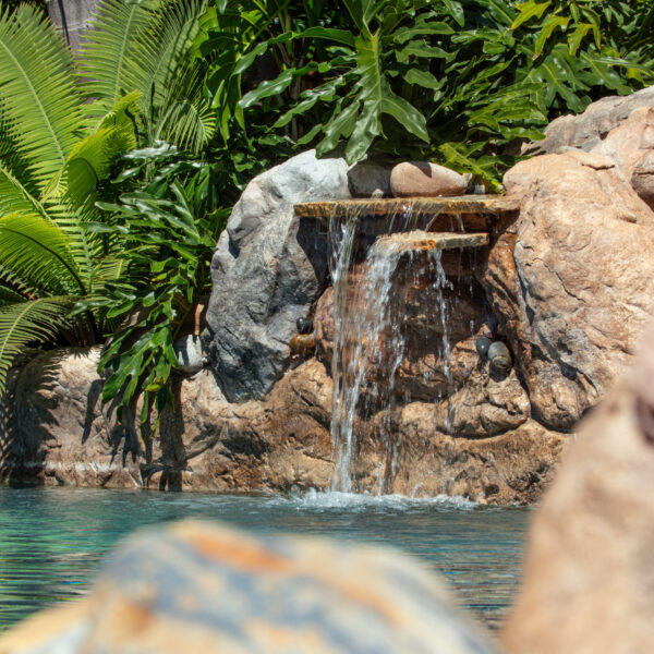 Detailed shot of waterfall and blue lagoon water with tropical foliage behind and rock cropping in the foreground at Tropic Shots production set